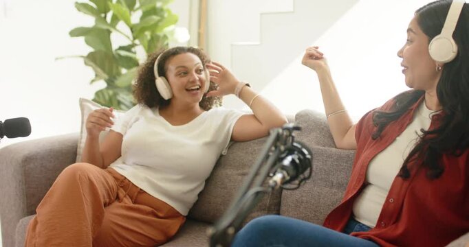 Diverse female friends reacting to mic, laughing and rehearsing podcast on couch recording episode