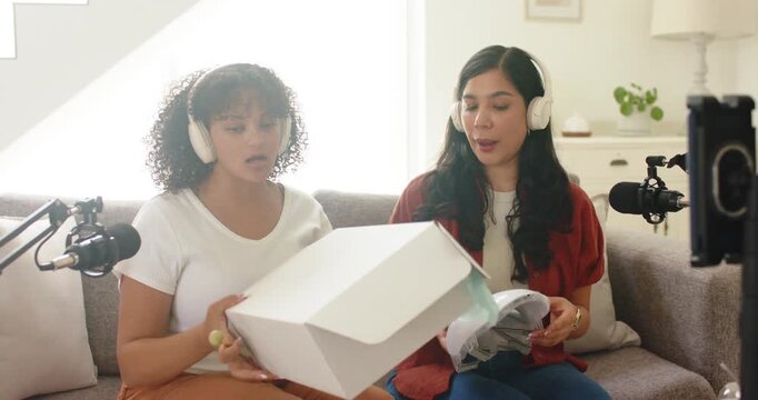 Two women sitting on couch, left woman opening white box, revealing applicator sticks for review