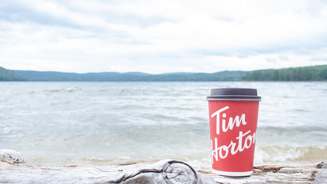 Tim Hortons coffee cup on log by lake with cloudy sky and green forest in the background