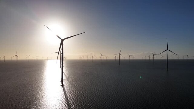 Leftward drone sweep across offshore turbines at sunrise