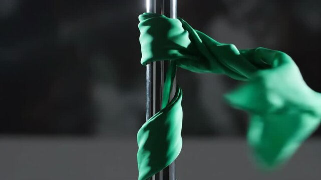 Green fabric wrapped around a silver pole in a dark setting.