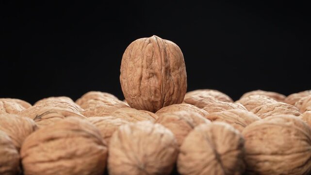 Cinematic rotating macro of a single prominent walnut standing on a pile with shallow depth of field on a black background. Premium nutrition concept.