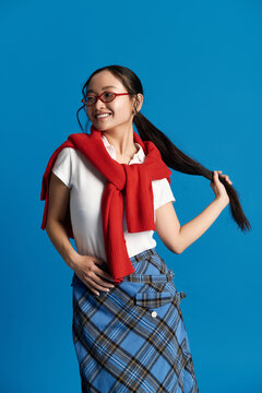 Stylish young asian woman with playful charm showcases vibrant fashion against bright blue backdrop