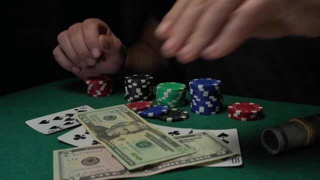 A male gambler with visible hands throws cash onto playing cards with a winning combination of two pairs on a green felt table, creating a focused atmosphere in the gaming environment