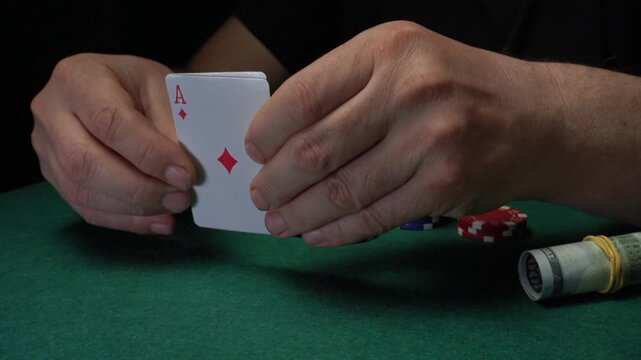 Player's hands skillfully reveal poker cards with three aces or set surrounded by colorful poker chips and cash on a green felt table in a gaming setting