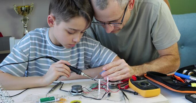 Father and son work together on electronics project. Dad and kid solder components and connect wires. This collaborative activity fosters learning and creativity. Enjoy quality time while building