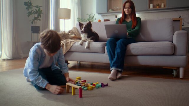 Boy builds colorful blocks while woman works on laptop at home