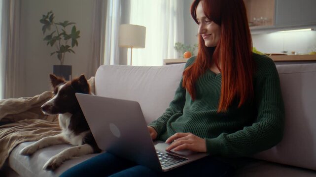 Woman works on laptop while dog rests close on sofa at home