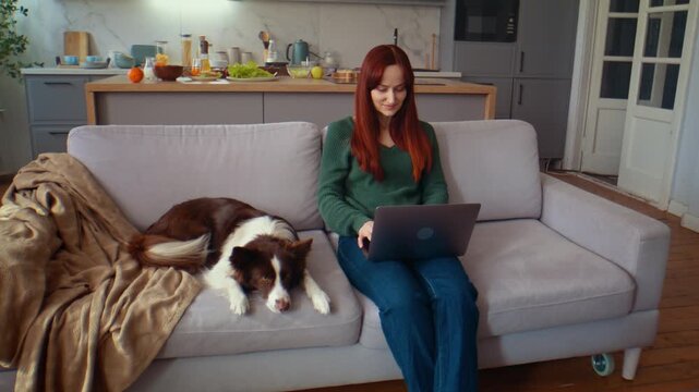 Woman works on laptop while dog rests on cozy sofa at home