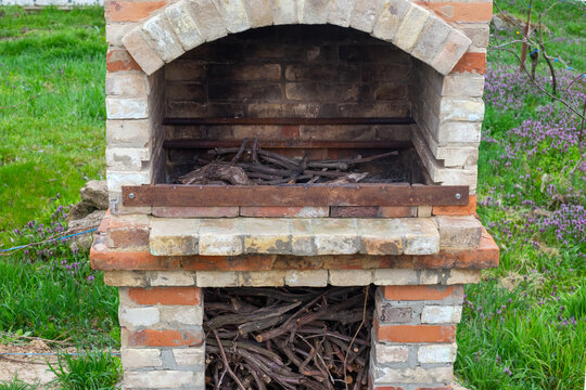 A rustic outdoor brick barbecue oven stands on green grass. Outdoor cooking area, garden stone grill, backyard patio station.