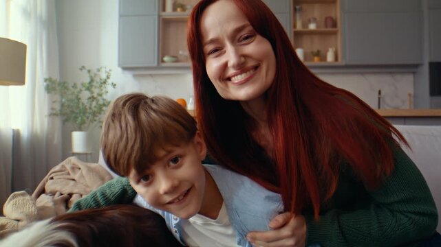 Woman hugs boy and dog in playful close moment on home sofa