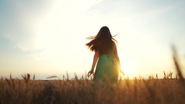 A girl runs around a farm in a wheat field at sunset. Freedom happiness women's rights concept. A woman runs for freedom at sunset. A woman in a green dress run through a field lifestyle.