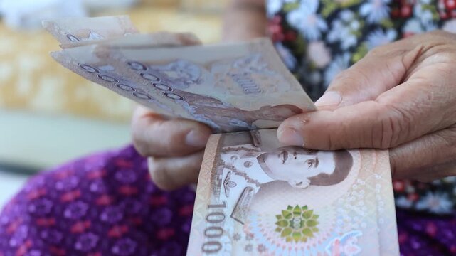 Elderly hands counting Thai banknotes Baht, Money close-up. Concept of retirement savings, pension income, financial security, budgeting, and senior financial planning