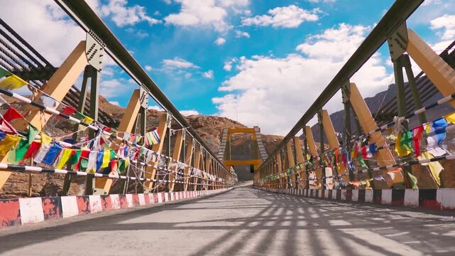 Buddhist prayer flags waving at Chicham Bridge in Spiti valley at Himachal Pradesh, India. Fluffy clouds in blue sky above Chicham bridge during summer season. Highest suspension bridge of Asia.