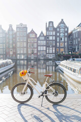 Fototapeta premium White Bicycle with Flowers on Damrak Waterfront with Traditional Dutch Dancing Houses in Amsterdam