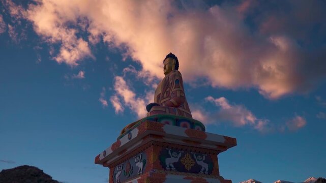 Tall Statue of Buddha against sunset sky at Langza, Spiti Valley, India. Silhouette of Buddha and orange clouds in sky. Travel landmark concept. Gautam Buddha statue.