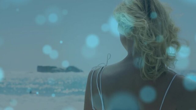 Model posing at beach on fashion cue, turning and smiling while turquoise bokeh drifting across