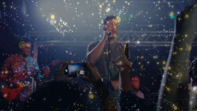 Vertical video: Lead vocalist starting music onstage, audience raising phones capturing gold bokeh