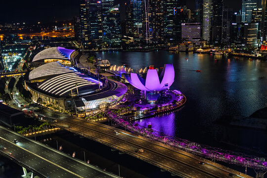 Nachtaufnahme vom Singapour Flyer auf die Dachkonstruktion von The Shoppes at Marina Bay Sands , das lila angestrahlte ArtSciende Museum und die Helix-Br&uuml;cke; im Hintergrund die Skyline von Singapur