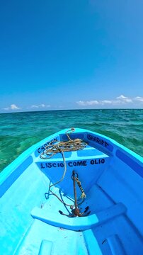 POV view from the bow of a blue wooden boat moving across turquoise water under a clear sky in Watamu, Kenya.