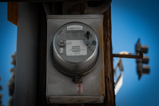 Close-up of a digital electric meter mounted on a utility pole against a bright blue sky