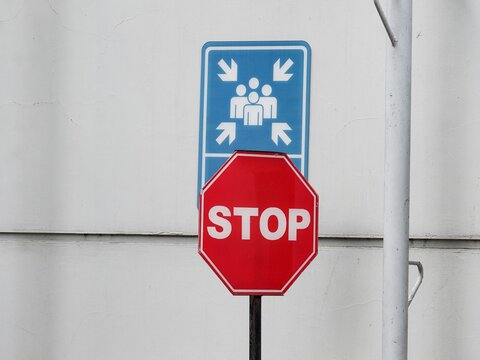 Dual safety signage featuring a muster point symbol and a stop command. This high-visibility combination is used for emergency management and directing personnel during building evacuations.