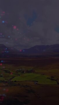 Vertical video: Light specks starting left drifting across valley fields, adding moody overlay