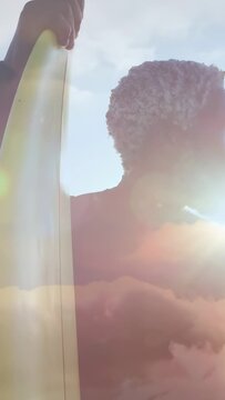 Senior surfer holding board turning to sun glare, motion flare tracking board while scanning sea