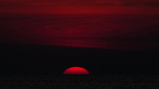 Golden sunset over the sea, captured from a scenic viewpoint. The sun slowly dips below the horizon, casting warm orange and yellow tones. Peaceful and serene atmosphere