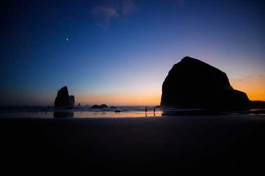 Sunset over Cannon Beach, Oregon. Vibrant sky, ocean waves, and the iconic Haystack Rock silhouetted against the evening light.