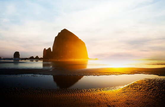 Sunset over Cannon Beach, Oregon. Vibrant sky, ocean waves, and the iconic Haystack Rock silhouetted against the evening light.