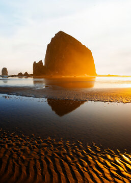 Sunset over Cannon Beach, Oregon. Vibrant sky, ocean waves, and the iconic Haystack Rock silhouetted against the evening light.
