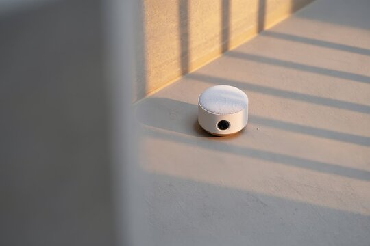 Small white speaker sitting on a gray surface in a room with sunlight streaming through blinds