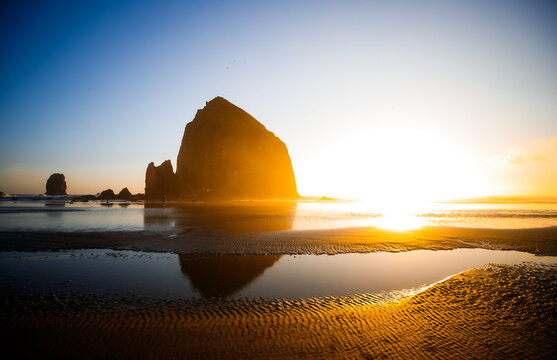 Sunset over Cannon Beach, Oregon. Vibrant sky, ocean waves, and the iconic Haystack Rock silhouetted against the evening light.