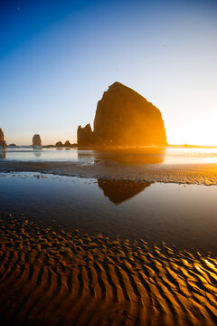 Sunset over Cannon Beach, Oregon. Vibrant sky, ocean waves, and the iconic Haystack Rock silhouetted against the evening light.