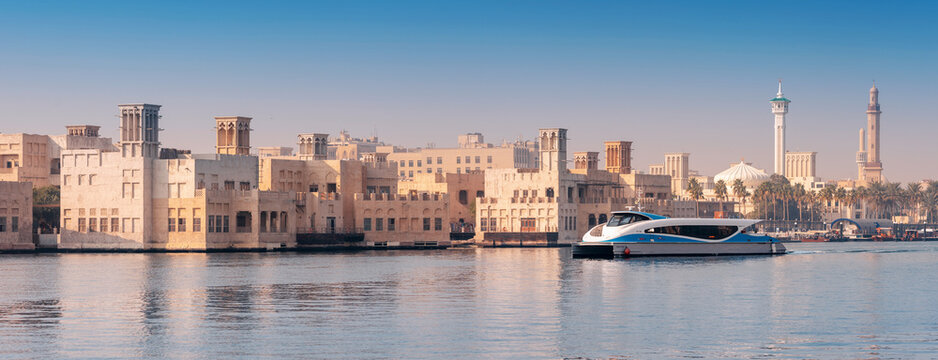 12 January 2026, Dubai, UAE: Modern RTA ferry boat traveling across Creek with traditional minarets, palm trees, and historic architecture lining the shore