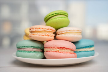 Obraz premium close-up of a pastel macaron tower on a white plate in a bright, airy studio or cafe setting; delicate pink, mint, blue, yellow and cream confections stacked, softly lit with shallow bokeh backdrop