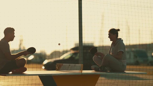 Couple sitting on a table playing ping pong at sunset