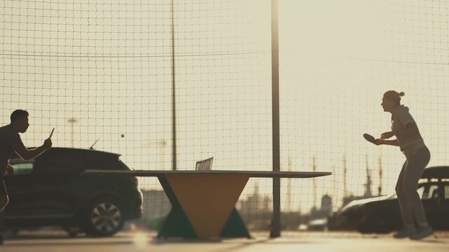 Silhouette of couple playing ping pong outdoors at sunset
