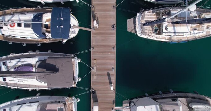 Overhead View Of Yachts Moored Along Pier With Lone Dockhand Walking, Turquoise Water, Calm Reflections And Orderly Berths Creating Geometric Pattern