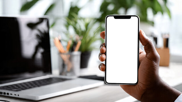 Main tenant un smartphone avec &eacute;cran blanc avec arri&egrave;re plan de bureau	personnel avec ordinateur portable et plantes