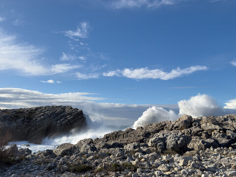 Atlantic wave energy creating sequential impact along rocky coast. Foam disperses into fine spray under deep blue sky with natural copy space for banner background