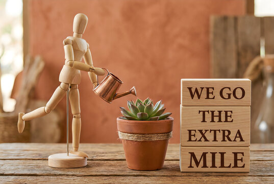 Mannequin with watering can near "we go the extra mile" blocks, a wooden artist's mannequin