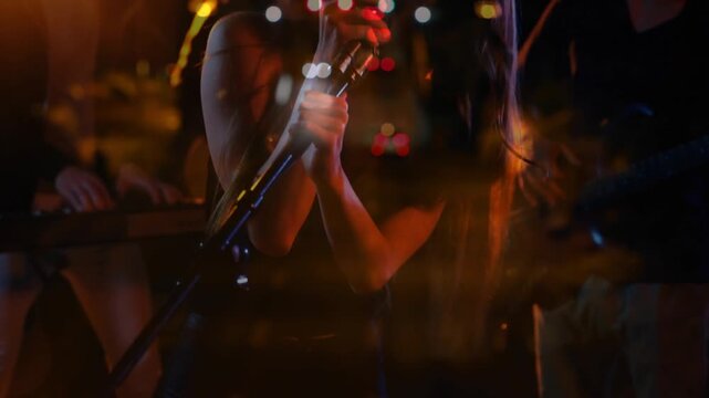 Camera revealing female singer singing holding chrome mic taillight bokeh layering band playing