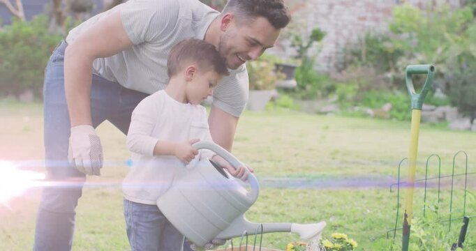 Father guiding son tipping gray watering can in backyard gardening, watering yellow flowers