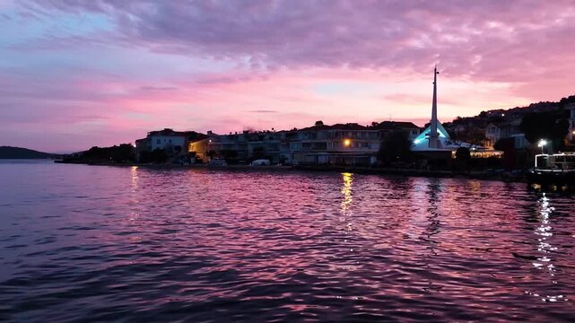 A breathtaking wide-angle view of the Marmara Sea coastline from Kınalı Island in Istanbul. During a magnificent pink and purple sunset, a unique modern mosque and the town lights are reflected on the