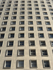Fototapeta premium Minimalist building facade with repetitive square windows pattern and geometric shadows