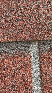 Close-up red hexagonal shingles texture, flexible asphalt roofing with coarse granules, overlapping pattern with subtle weathering.