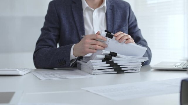 Business professional sorting a large stack of financial reports and tax forms with binder clips on a busy office desk. Audit and taxes