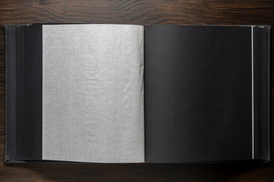 Empty black photo album pages with translucent interleaves on dark wood. Mockup for wedding portfolio, memory book, or elegant branding presentation. Top view.